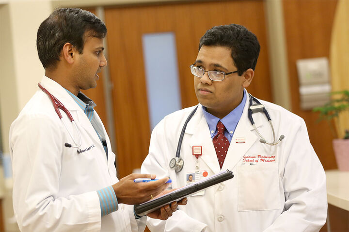 A medical professional holding a tablet speaks with a medical student.